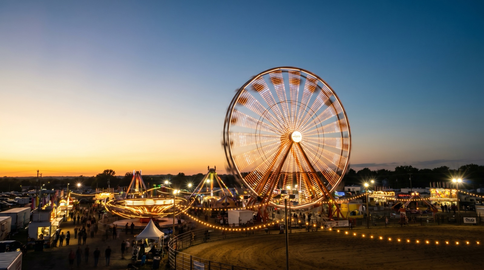 Wide photographic view of a summer rodeo and fairground at dusk, a large illuminated ferris wheel and midway lights, no logos, no signage, no recognizable people