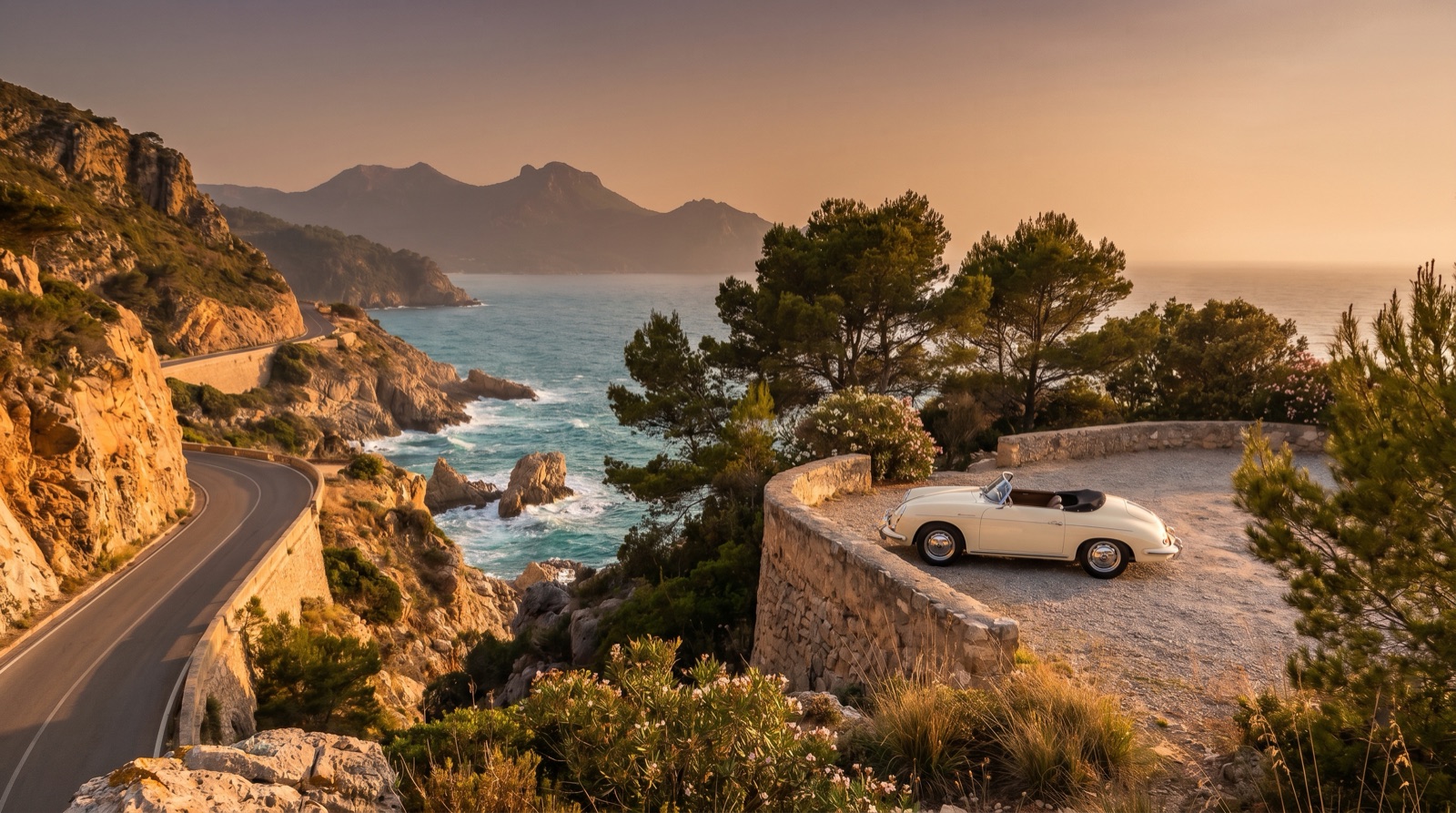 A coastal road winding along seaside cliffs at golden hour with turquoise water below, distant mountains, and a vintage convertible parked at a scenic stone overlook