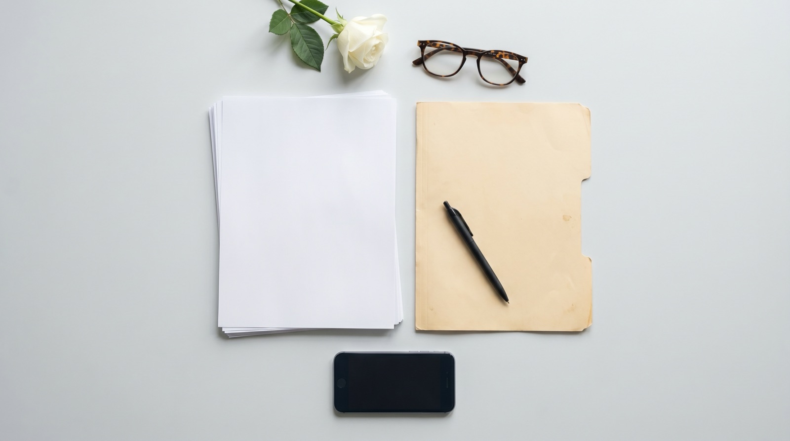 A tidy flat-lay on a pale gray desk with a neat stack of blank white documents, a manila folder, a pen, reading glasses, a single white rose, and a face-down smartphone in soft even light